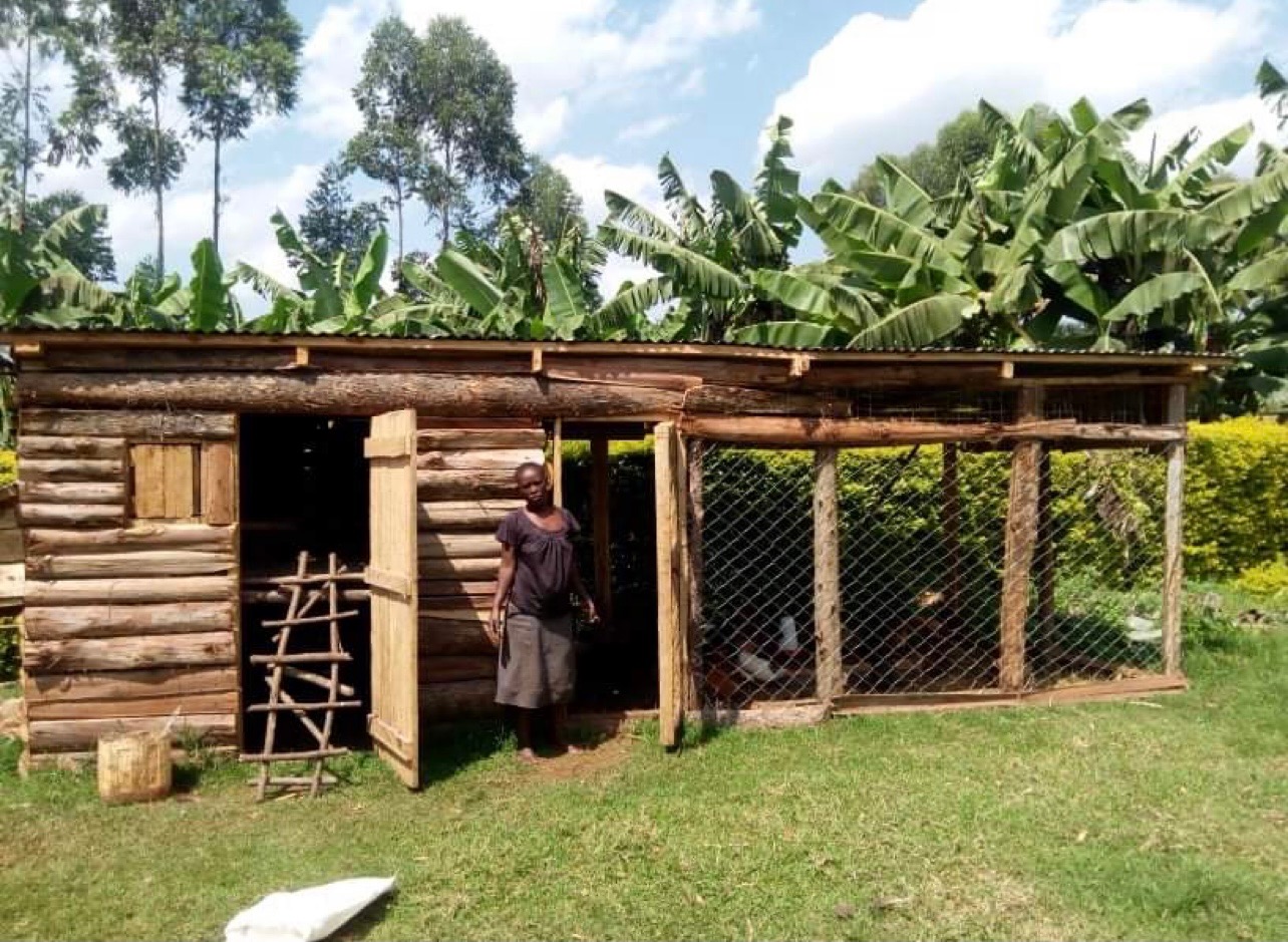 A community member standing beside a wooden chicken coop supported by Roots to Rise
